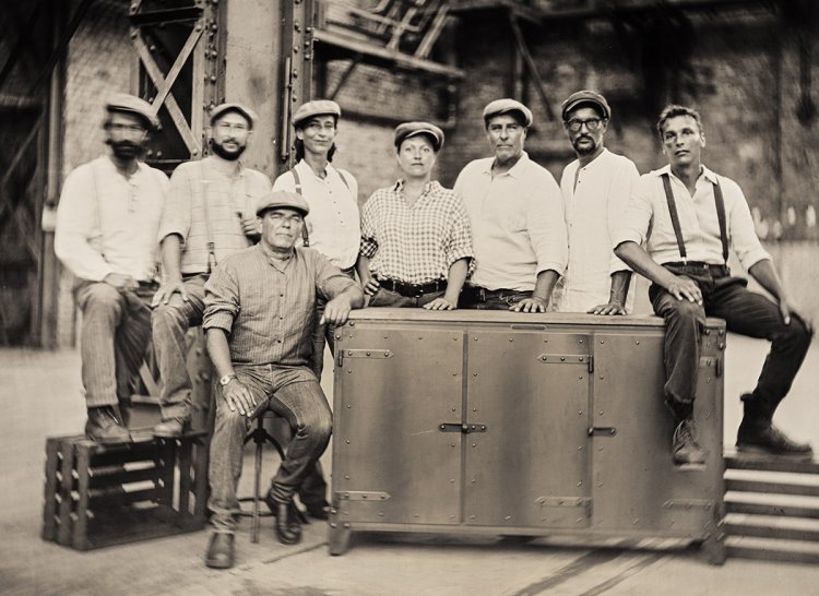 Team von Noodles Noodles & Noodles Corp. posieren mit altmodischen Hüten in einer alten Fabrikhalle. Das Bild ist schwarz-weiss mit einem Sepia-Ton.