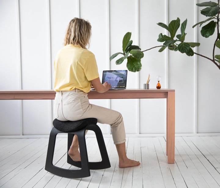 Frau auf schwarzem Muista-Schaukelstuhl an Holzschreibtisch mit Laptop
