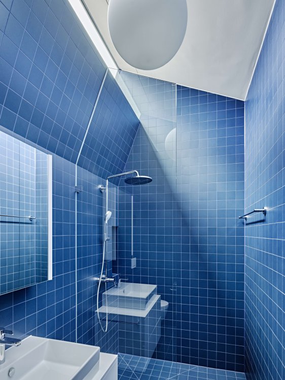 Bad mit angewinkeltem Dach, von wo Licht einfällt, vollständig mit dunkelblauen Fliesen ausgekleidet.