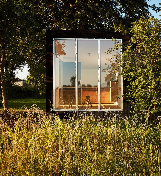 Black Cabin Ansicht von vorne mit Glasfront, umgeben von Wiese.