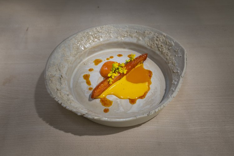 Weisser Teller mit einer Karotte gebraten in der Mitte, darüber gelb-orange Sauce.