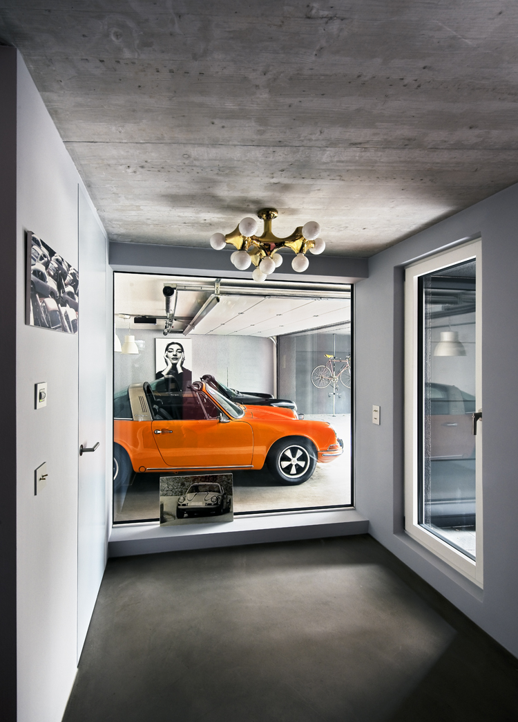 Blick durch bodenlanges Fenster von Entree in die Garage auf einen orangen 911er-Porsche.