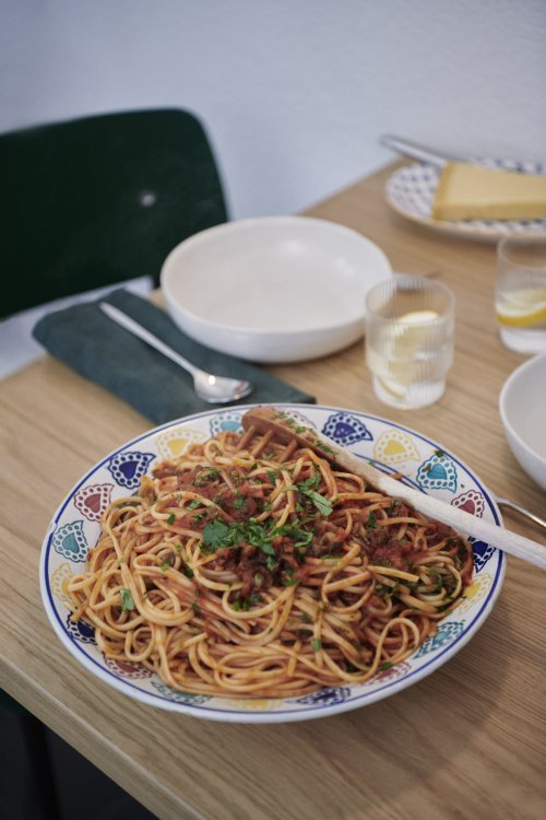 Tomatensphaghetti zubereitet auf einem Teller mit farbigem Muster am Rand auf einem gedeckten Tisch.