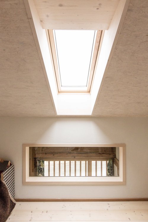 Dachfenster in einer Dachschräge aus Holz, darunter ein flaches Fenster beinahe auf Bodenhöhe, das Licht ins untere Zimmer lässt.