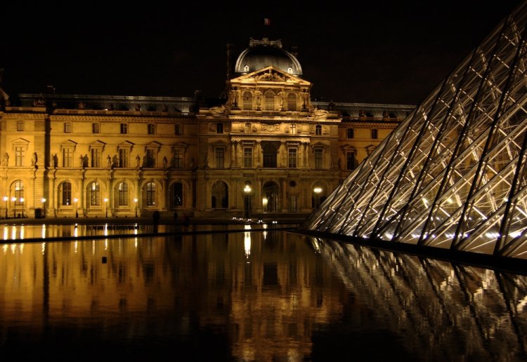 Beleuchteter Haupteingang des Louvre bei Nacht.