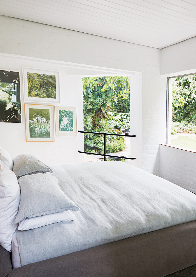 Schlafzimmer mit Blick ins Grüne, Bett ist mit weisser Bettwäsche bezogen, an der Wand link hängen stimmungsvolle Bilder.