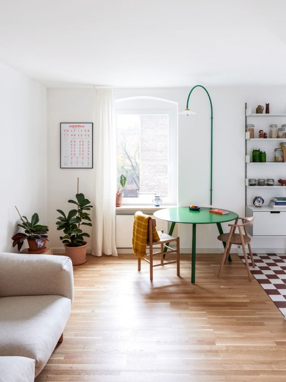 Blick ins Wohnzimmer mit Parkettboden, helles Stoffsofa auf linker Seite und grünem, runden Küchentisch.