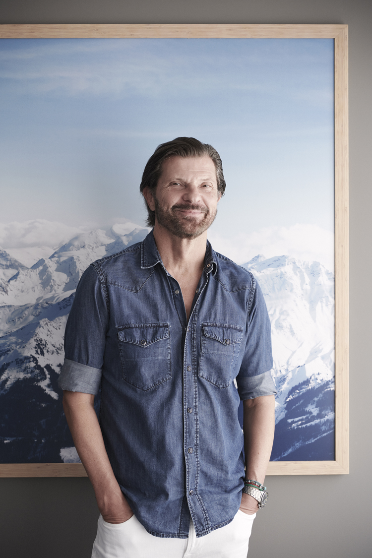 Erhard Schwendimann steht vor einem grossen Bergpanoramabild in einem Jeanshemd.