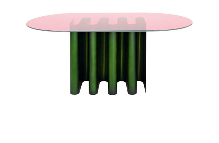 Ovaler Beistelltisch mit gläserner Tischplatte in rosa und grünem Sockel in from eines aufgestellten Wellblechs.