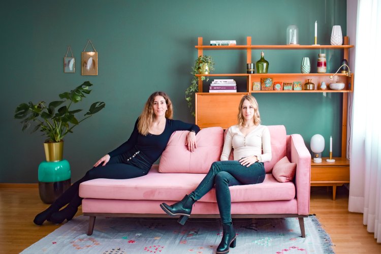 Selina von Matt und Anja Hofmeier sitzen auf einem rosa Sofa vor einer grünen Wand.