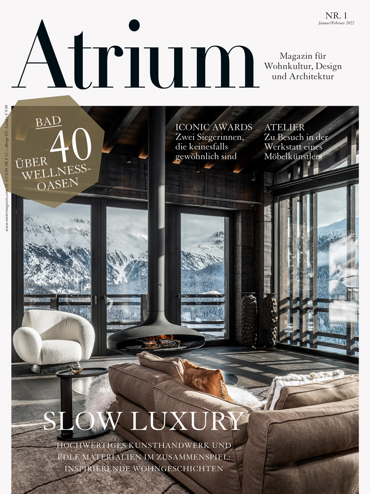 Titelblatt Atrium Magazin Ausgabe 1 von 2022 mit einem Bild von Innenansicht Wohnzimmer mit hängendem schwarzen Cheminée in Chalet-Villa in St. Moritz mit Blick in die Winterlandschaft.