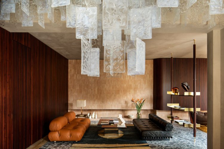 Blick in den Wohnbereich im Art-Deco-Stil mit einer Holzwand in Nussbaum und einem caramelfarbenen Sofa und einem schwarzen Ledersofa.