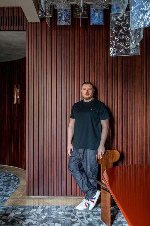 Architekt Hannes Peer steht angelehnt an einer Holzwand in Jeans und schwarzem T-Shirt.