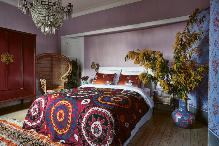 Schlafzimmer im rot-rosa Bohemian-Style mit rosa Wänden und einem zentrierten Doppelbett mit Tagesdecke.