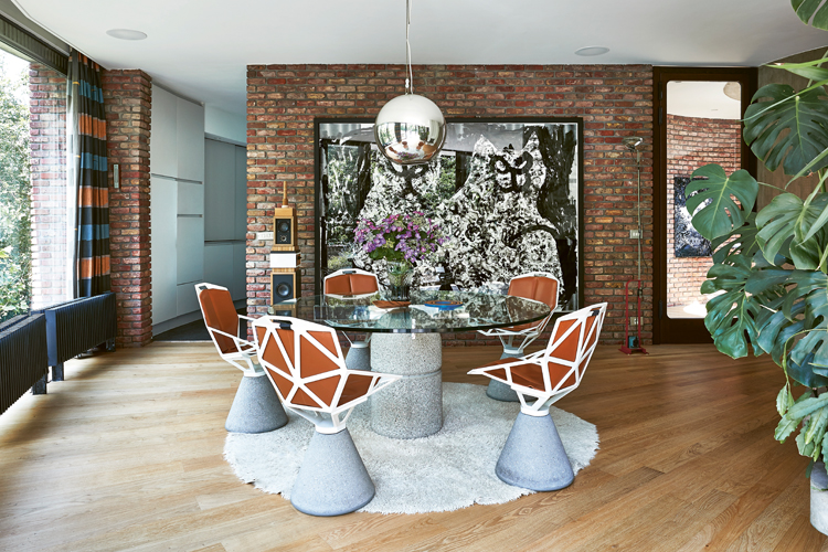 Massiver runder Esszimmertisch aus Glas mit Betonsockel und vier auffälligen skulpturalen Stühlen in einem Backsteinraum.