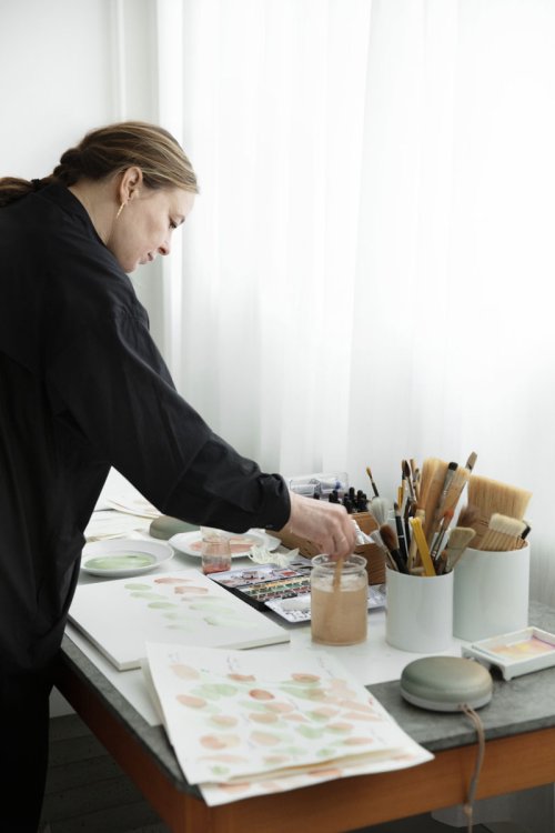 Designerin Cecilie Manz in schwarzer Bluse malt einige Farbskizzen auf Papier.