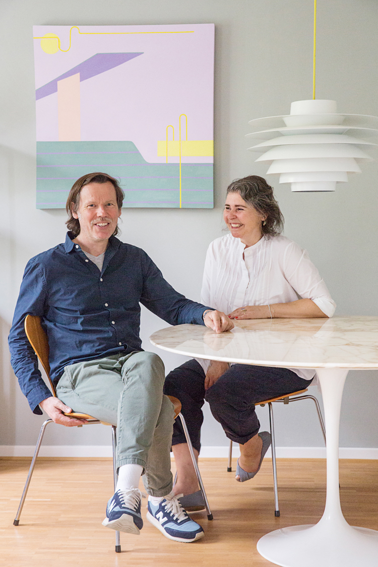 Frank und Yasmin Mevissen sitzen an einem weissen runden Tisch von Knoll vor mintgrüner Wand mit buntem Bild.