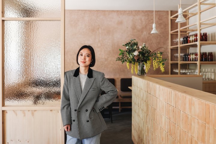 Fan Xiaofen Inhaberin des Restaurants Ryke in Berlin steht vor dem Tresen mit schwarz-weiss kariertem Blazer.