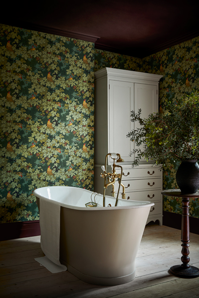 Badezimmer mit floraler Tapete in Olivgrün und weisser freistehender Badewanne im Vordergrund.
