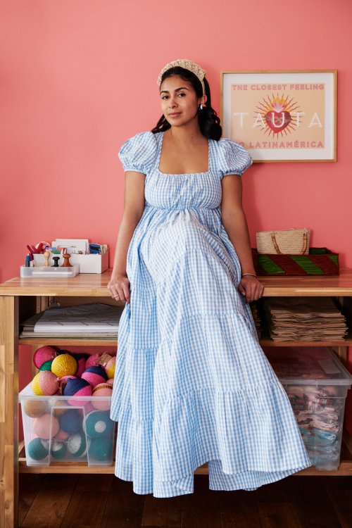 Maria Bezzola-Lorez sitzt auf ihrem Tisch mit blau-weissem langem Kleid vor lachsfarbener Wand.