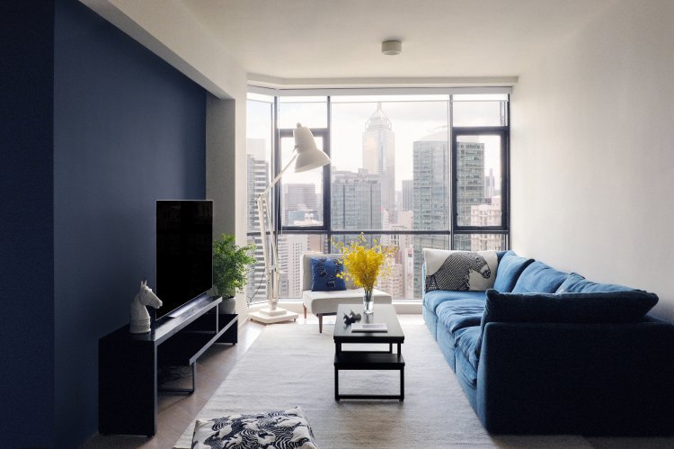 Wohnzimmer mit blauer Wand, grosser Fensterfront mit Aussicht auf Hongkong und einem blauen Samtsofa.