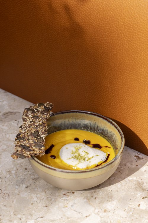 Dickflüssige Kürbis-Suppe in einer braunen Schüssel vor oranger Wand.