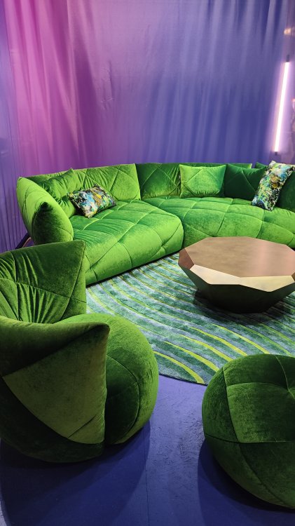 Ein Foto mehreren grünen Sofas die auf einen grün bemusterten Teppich stehen. In der Mitte der Lounge steht ein runder Beistelltisch.