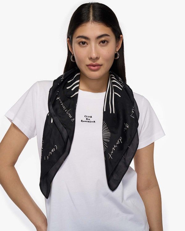 Model mit offenen langen dunklen Haaren und weissem T-Shirt und schwarzem Foulard um den Hals.