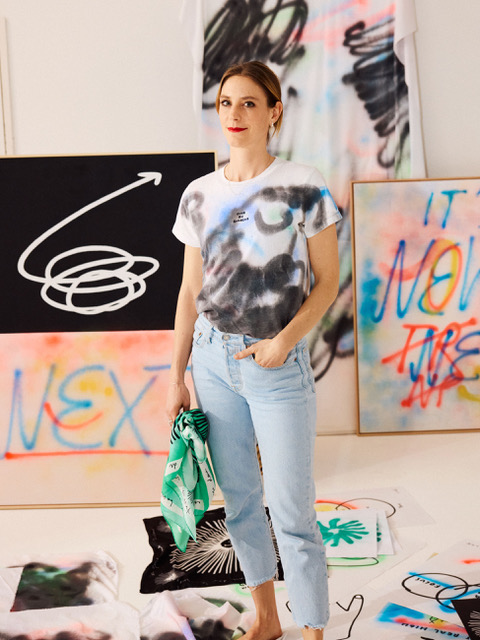 Die Designerin Simone Züger steht vor besprayten Bildern in Jeans und einem weiss-schwarzen T-Shirt..