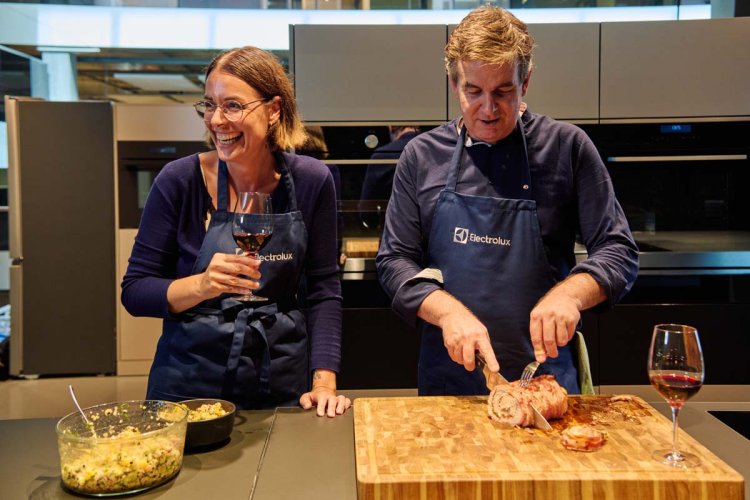 Zwei Menschen in der Küche. Einer trinkt Wein, der andere schneidet Fleisch.