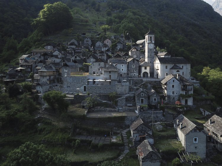 Blick auf das steil an einen Hang gebaute Tessiner Dorf Corippo mit engen Gassen, kompakt gebauten Steinhäusern und einer Kirche.
