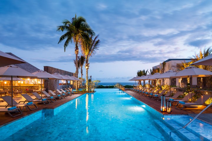 Ein beleuchtenden Pool am Abend der von Palmen und Liegestühlen umgeben ist.