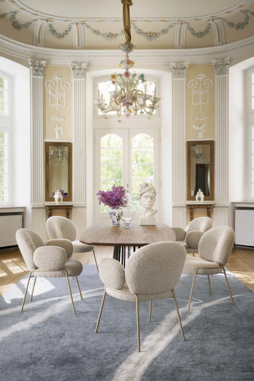 Ein Foto eines Esszimmers. Zu sehen ist ein brauner ovalen Tisch mit weissen bequemen Stühlen.