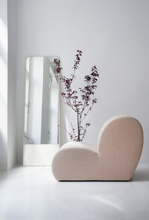 Ein rosa, organisch geformtes Sitzobjekt Levi steht in einem weissen, schlichten Raum vor einer lila Pflanze und einem langen Spiegel.