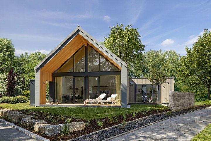 Aussenansicht des neuen Musterhaus "Freiraum" von Baufritz mit vorgezogenem Dach und grossflächiger Glasfassade steht in einem kompakten grünen Garten.