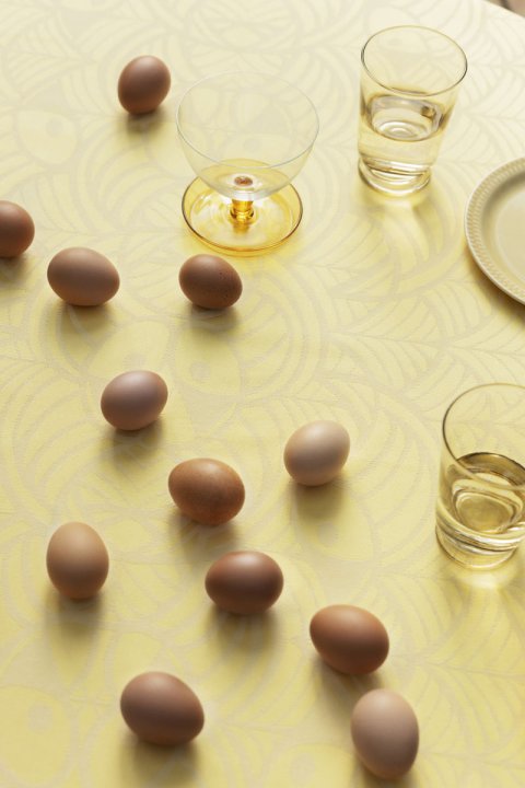 Ein gelbes Tischtuch mit Muster auf dem kleine Schokoliere neben Wein- und Wassergläsern liegen.
