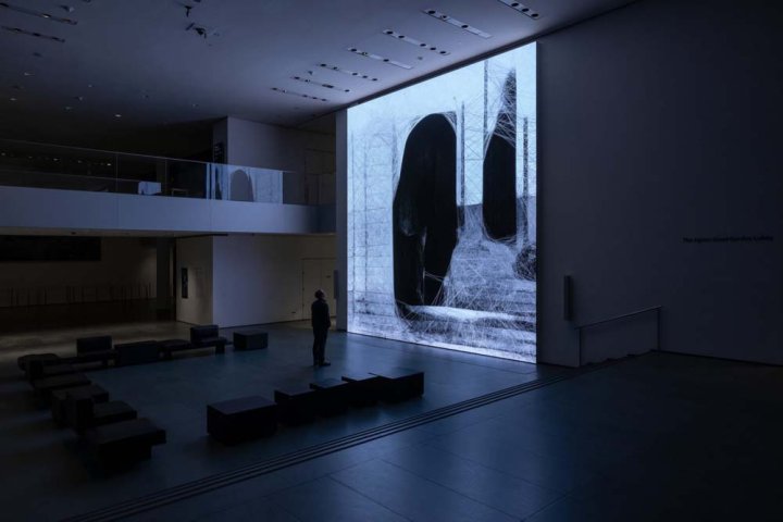 Ein Besucher steht im Entree des Museum of Modern Art in New York vor einer quadratischen Animation in blauen Farben, welche in den dunklen Saal des Museums strahlt.