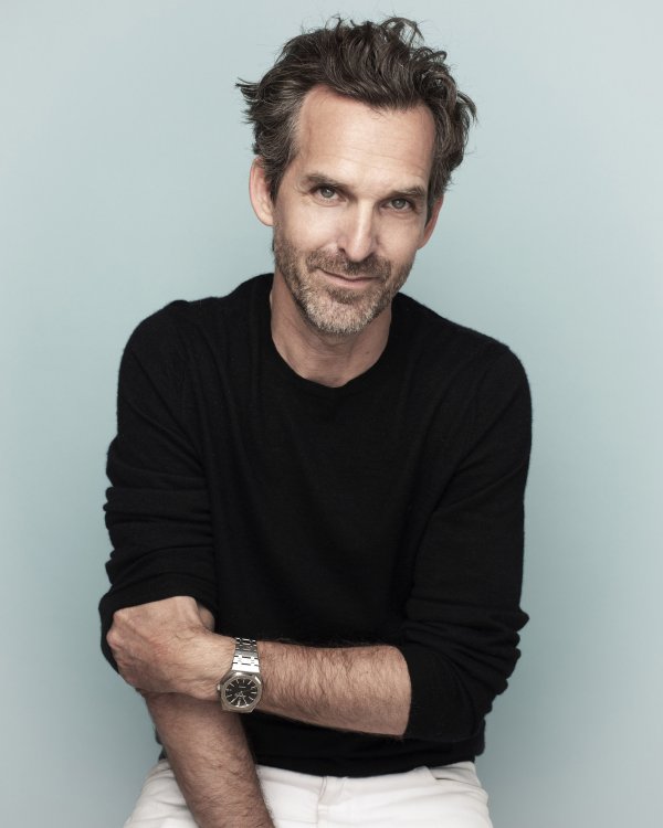 Der französische Designer Mathieu Lehanneur in schwarzem Pullover und weisser Hose vor einem türkisblauen Hintergrund.